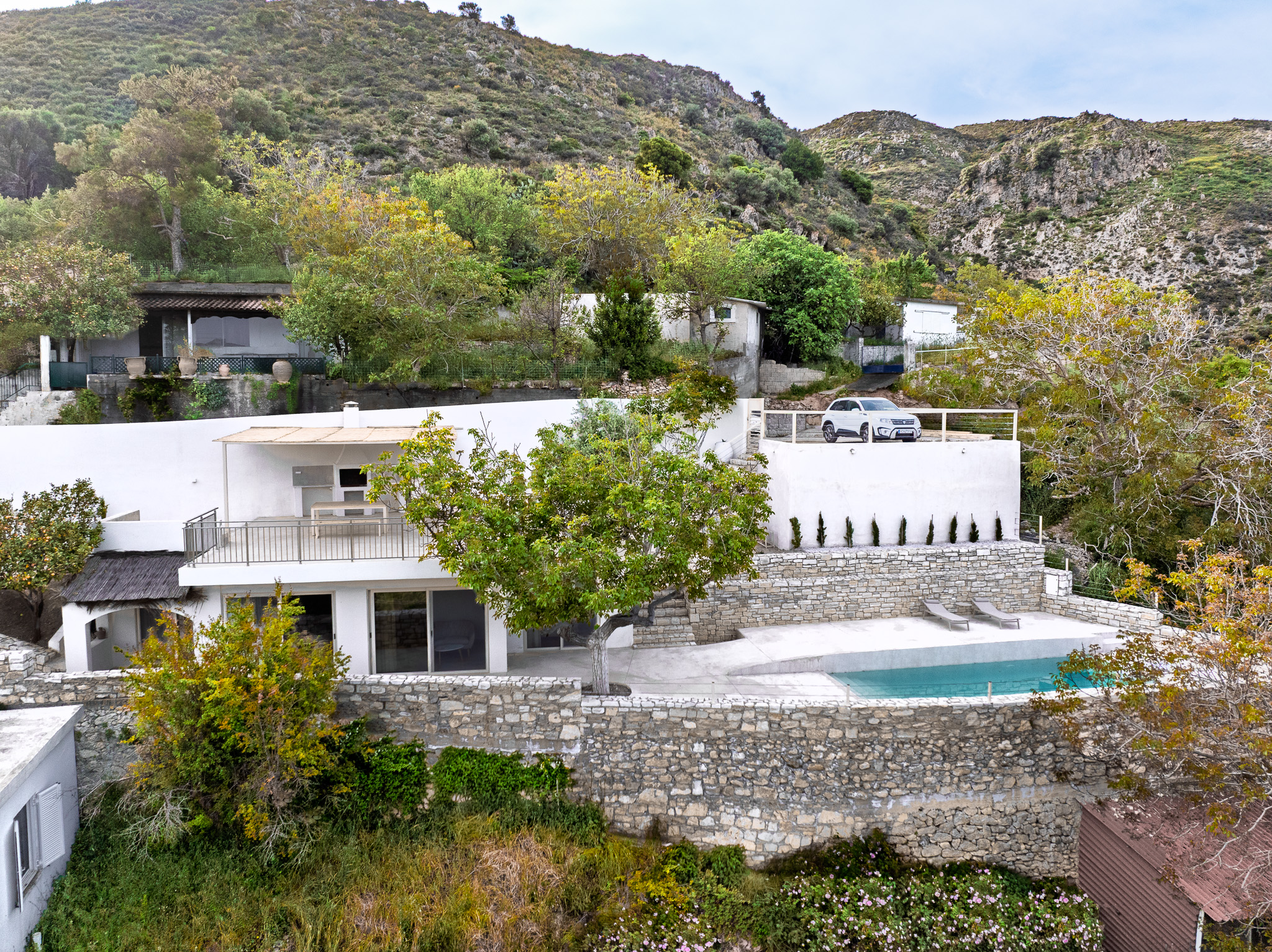 Wide view of Nogal Retreat, pool, stone walls, trees, and hillside